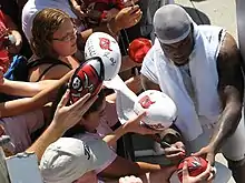 African American male in stocking cap signs autographs for fans on footballs