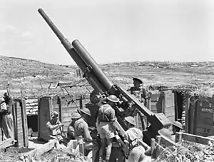 Black and white photograph of several men wearing military uniforms standing next to a large artillery gun