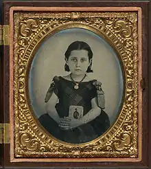 Girl in mourning dress holding framed photograph of her father, USA, encased, c. 1861–1870