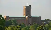 tall and long red brick cathedral with green roofs and square tower topped with gold angel