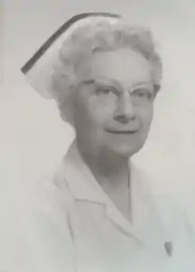 Image of a middle-aged woman wearing spectacles, a white nurse's cap, and a white coat