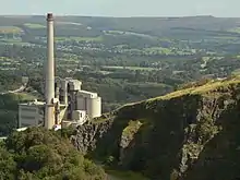 A large chimney set in a deep valley, surrounded by hills, trees and old quarrys