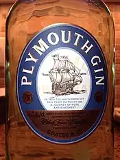 Close-up of bottle showing an oval label. Title "Plymouth Gin" in white capital letters placed curvilinearly around top edge of the oval, all in a wide blue band that borders the label. In the centre of the oval is a smaller white oval on which is a line drawing of a fully rigged sailing vessel. Below this in smaller blue type is: "In 1620 the Mayflower set sail from Plymouth on a journey of hope and discovery". The base of the oval has a gold-coloured section, with black type not clearly legible in the image, except that a company name "Coates & Co." in plain type can be seen, with "Black Friars distillery" in cursive script above that.