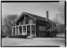A 3 and a half story building sided with wooden shingles. There is a porch with white pillars at the front of the building.