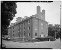 A photograph of a four-and-a-half-story brick building with a pitched room and two chimneys on its near end