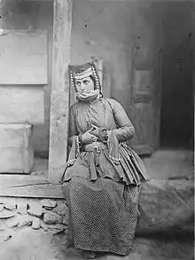 Menina Udi em trajes nacionais de Vartashen (hoje Oguz). Está sentada em frente a uma casa.