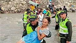 Migrantes venezuelanos cruzando um rio, auxiliados pela polícia colombiana