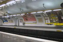 Detalhe de uma plataforma, com todas as instalações Ouï-dire: rampa luminosa suspensa por consoles curvos (ou "foices"), assentos individuais ou banco assis-debout e friso publicitário amarelos e telhas brancas planas.