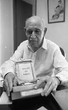Amaral Gurgel em idade avançada segurando o troféu onde se lê "Ídolos do Rádio".