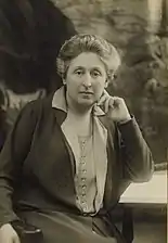 A posed black and white photograph of a woman seated at a desk