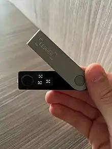 Mão segurando uma carteira hardware Ledger Nano X sobre fundo de madeira