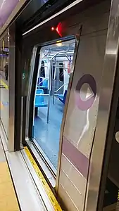 Na imagem, temos o exterior de um trem da Frota F parado com suas portas abertas na estação Adolfo Pinheiro, visto de lado. Ele apresenta o padrão roxo da ViaMobilidade Linhas 5 e 17 e tem o seu indicador de fechamento de portas aceso. Nota-se sua nova pintura, assim como os novos pega-mãos lilases, ao fundo o novo mapa da linha e mais à frente os bancos com seu estofado removido e substituído por plástico duro.