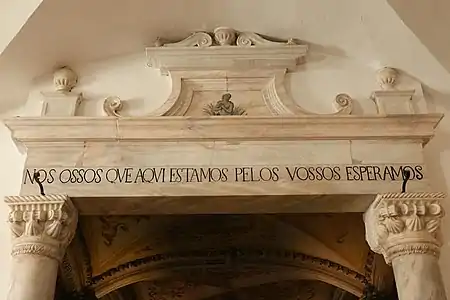 Inscrição sobre a porta de entrada: "Nós ossos que aqui estamos pelos vossos esperamos."