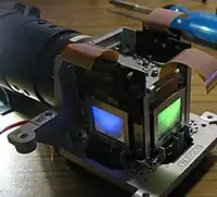 Parte do conjunto ótico de um projetor LCD. À mostra os painéis LCD e lente objetiva (à esquerda).