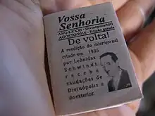 Micro jornal posicionado sobre a palma de uma mão, ocupando pouco espaço.