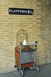 Uma placa escrito "Plataforma 9¾" com a metade de um carrinho na parede.