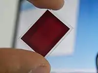 Um dos polarizadores presentes em um projetor 3LCD. Note o pequeno tamanho e o notável desgaste com o uso presente no componente.