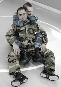 Em um campo, um militar está fazendo o Mata-Leão.