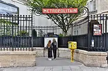 Vue de l'entrée de la station avec un plan du métro que deux personnes consultent.