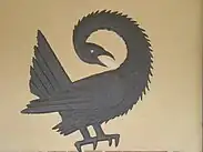 pássaro sankofa preto esculpido em uma superfície plana e clara, provavelmente uma parede.