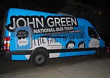 Um vã em azul com uma imagem da capa do livro e a promoção "John Green National Bus Tour".