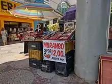 Barraca de vendedor ambulante de morango com placa escrito "Morango - 3 por 12 reais - Aceito pix"