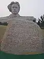 Inscrição na pedra e a estátua ao fundo.