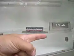Um vagão na escala Z, com o dedo de um homem próximo a ele para comparação de tamanho.